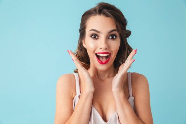 Surprised happy brunette woman in dress rejoices and looking at the camera over turquoise background clipart