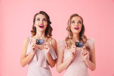 İki Surprised mutlu kadın kredi kartlarını tutarak ve pembe arka plan üzerinde ararken elbiseler