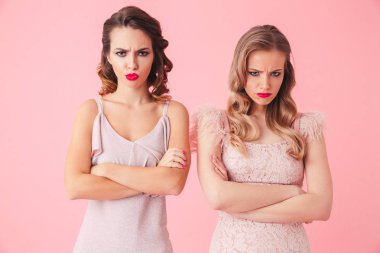 İki ciddi kameraya pembe arka plan üzerinde çapraz silahlarla seyir elbise kadınlarda sıktı