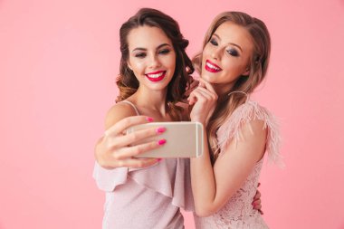 İki birlikte poz ve selfie smartphone üzerinde pembe arka plan yapma elbiseler şık kadınlar gülümseyen