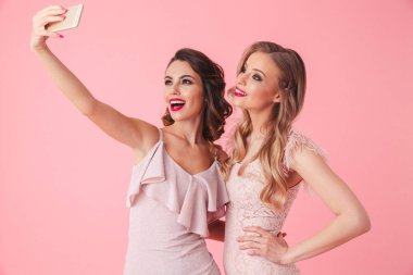 İki mutlu zarif kadın birlikte poz ve selfie smartphone üzerinde pembe arka plan yapma elbiseler