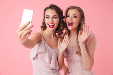 Pembe arka plan üzerinde izole kamera selfie fotoğrafta üstünde hareket eden telefon ve sallayarak 20'li yaşlarda el iki genç parti kadın fotoğrafı