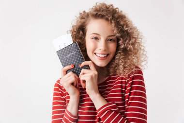 Kıvırcık saçlı beyaz arka plan üzerinde izole pasaport holding ile gülümseyen genç kız portre kadar yakın