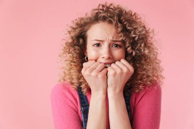 Kıvırcık saçlı pembe arka plan üzerinde izole kamera bakarak korkmuş genç kız portresi kapatın