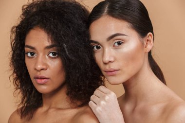 Güzellik Portresi iki çok ırklı kadın modelleri, makyaj poz olmadan Asya ve Afrika kökenli Amerikalı kadınlar birlikte bej renkli arka plan üzerinde izole