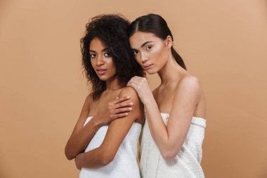 Güzellik Portresi iki çok ırklı yarım haked kadın modelleri, makyaj poz olmadan Asya ve Afrika kökenli Amerikalı kadınlar birlikte bej renkli arka plan üzerinde izole