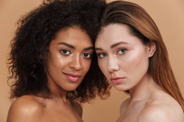 Güzellik portre portre iki farklı ulus kadın, doğal makyaj birlikte bej renkli arka plan üzerinde izole kamera poz ile. Afrikalı-Amerikalı ve beyaz kız
