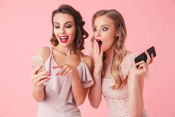 Дві Красиві Жінки Сукнях Стоять Разом Використовують Смартфон Рожевому Фоні — стокове фото