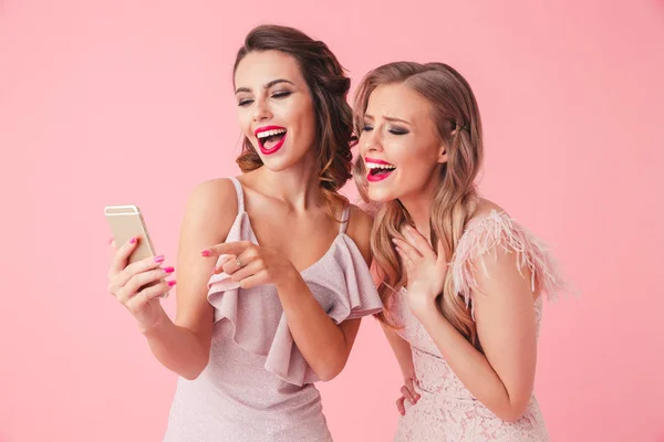 Две Веселые Элегантные Женщины Платьях Позируют Вместе Используют Смартфон Розовом — стоковое фото