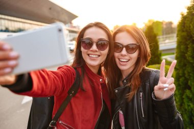 Görüntü closeup iki genç Avrupa kadın selfie smartphone Havaalanı bekleyen uçuş için veya ayrılmasından sonra yakın poz fotoğrafta güneş gözlüğü takıyor. Hava seyahat kavramı