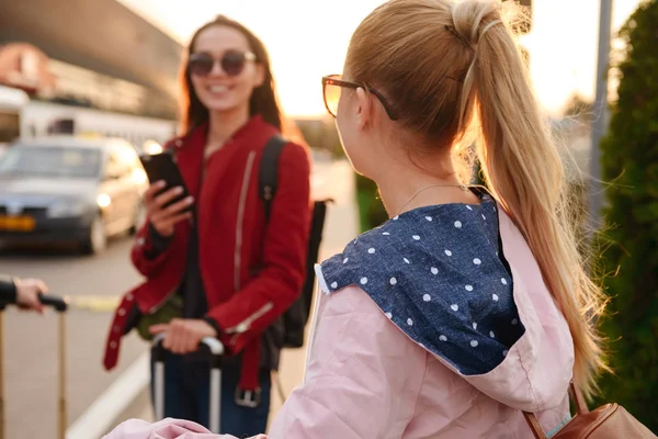 两名年轻妇女一起出国旅游的照片 并在等待机场附近的行李时使用手机 航空旅行或假日概念 — 图库照片