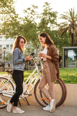İki genç güzel kadın arkadaşlar açık havada Bisiklet Park istimal hareket eden telefon ile görüntü.