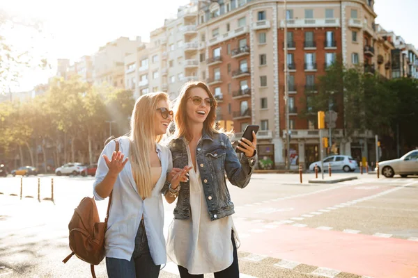 Bilden Två Fantastiska Kvinnor Vänner Promenader Utomhus Och Använda Mobiltelefon — Stockfoto