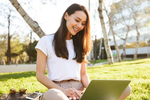 图片的华丽美丽的女人坐在草地上 在户外使用笔记本电脑 看一边 — 图库照片