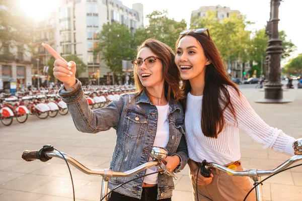 Imagem Duas Mulheres Bonitas Jovens Amigos Livre Bicicletas Rua Apontando — Fotografia de Stock