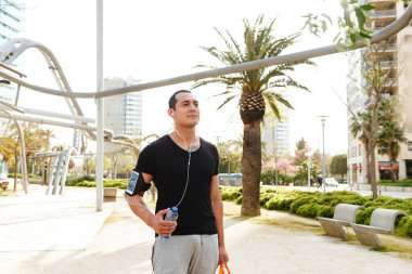 Açık havada su kulaklık ile müzik dinleme şişe ile yürüyen adam yakışıklı genç güçlü görüntü spor.