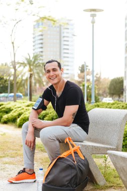 Yakışıklı genç güçlü görüntü adam açık havada dinleme müzik kulaklık ile spor. Görünümlü kamera.