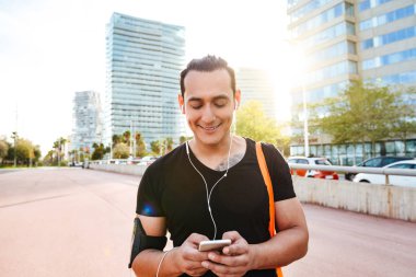 Mutlu genç güçlü spor adam açık havada cep telefonu dinleme müzik kullanarak yürüyor görüntüsünü.