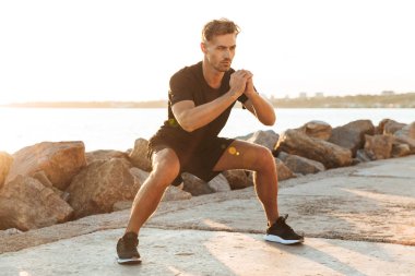 Yakışıklı güçlü konsantre sporcu görüntüsünü erken sabah sahilde açık havada spor egzersizleri yapmak.