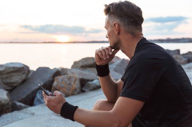 Plajda otururken cep telefonu kullanarak güçlü bir sporcu portresi