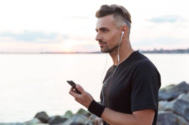 Kulaklık ile müzik dinlemek ve sahilde duran cep telefonu kullanarak uygun bir sporcu portresi