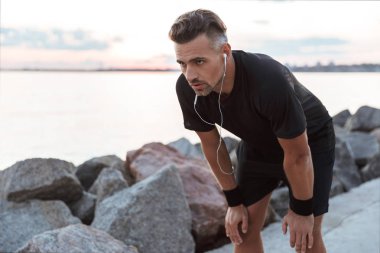Sahilde koşu sonra dinlenme sırasında kulaklık ile müzik dinlemek çok yorgun bir sporcu portresi