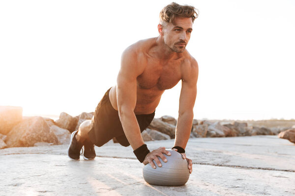 Портрет мотивированного спортсмена без рубашки, делающего упражнения с маленьким фитнес-мячом на открытом воздухе

