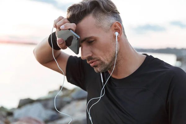 关闭在海滩慢跑后休息的疲惫的运动员的肖像听音乐与耳机 — 图库照片