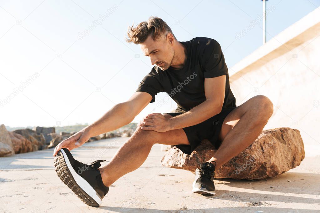 Portrait of a charming sportsman doing stretching exercises at the seaside in the morning