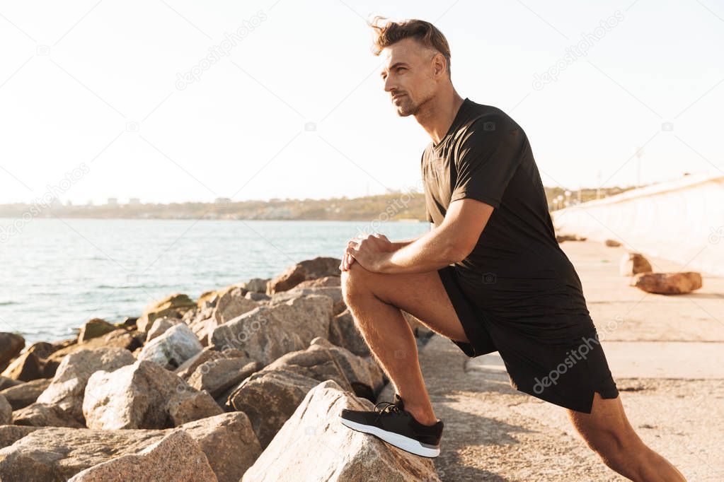 Portrait of a handsome sportsman doing stretching exercises at the seaside in the morning