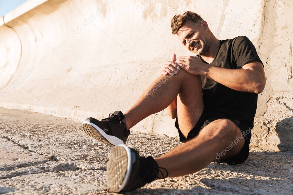 Portrait of an injured sportsman in pain suffering from knee pain while sitting outdoors