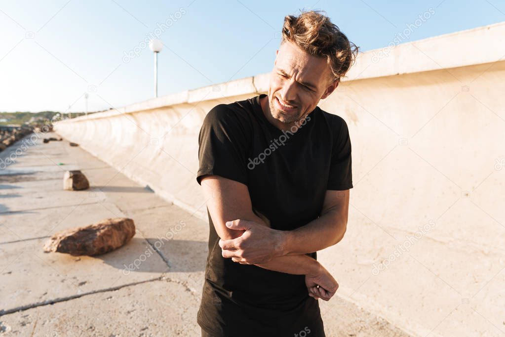 Portrait of an injured sportsman suffering from an elbow pain while standing outdoors