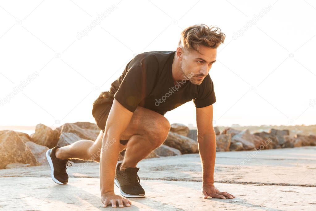 Image of handsome strong concentrated sportsman make sport exercises outdoors at the beach early morning.