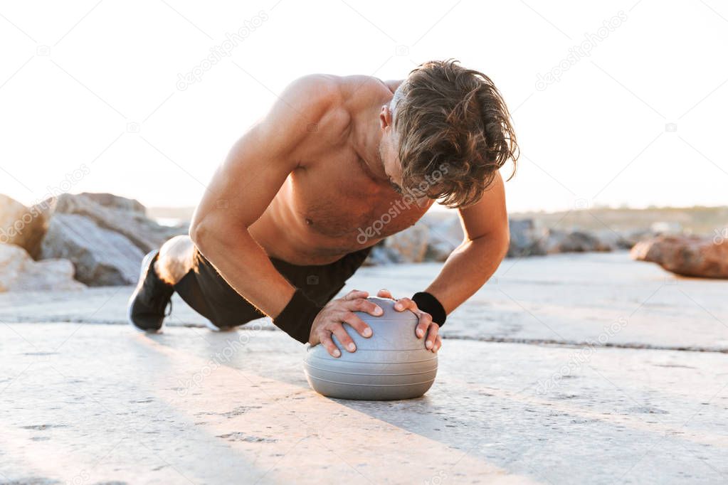 Portrait of a fit shirtless sportsman doing exercises with small fitness ball outdoors