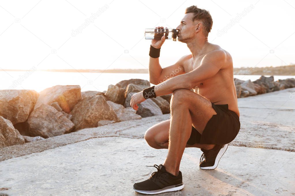 Portrait of a fit shirtless sportsman resting after jogging and drinking water outdoors