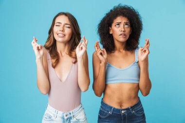 İyi şanslar üzerinde mavi arka plan izole için dua tutan yaz elbise giymiş iki endişeli genç kız