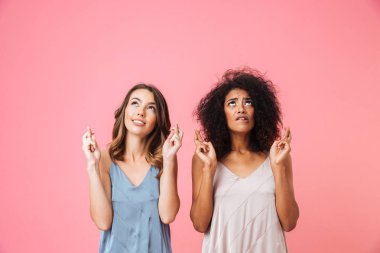 İyi şans getirmesi için geçti ve pembe arka plan üzerinde izole ararken parmak tutan yaz elbise giymiş iki endişeli genç kız