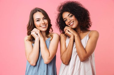 İki güzel genç kız ayakta ve pembe arka plan üzerinde izole kamera bakarak yaz elbise giymiş