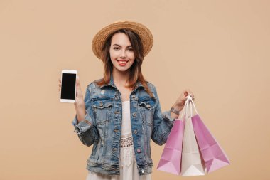 Boş ekran cep telefonu alışveriş torbaları bej renkli arka plan üzerinde izole tutarken gösterilen yaz giysileri neşeli bir genç kız portresi