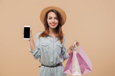 Boş ekran cep telefonu alışveriş torbaları bej renkli arka plan üzerinde izole tutarken gösterilen yaz giysileri neşeli bir genç kız portresi