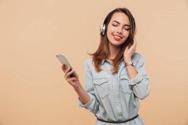 Cep telefonu bej renkli arka plan üzerinde izole tutarken kulaklık ile müzik dinlemek yaz giysileri gülümseyen genç bir kız portresi