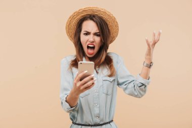 Cep telefonu bej renkli arka plan üzerinde izole bağırıyor yaz giysileri öfkeli bir genç kız portresi