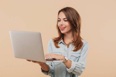 Bej renkli arka plan üzerinde izole dizüstü bilgisayar kullanan yaz giysileri neşeli bir genç kız portresi