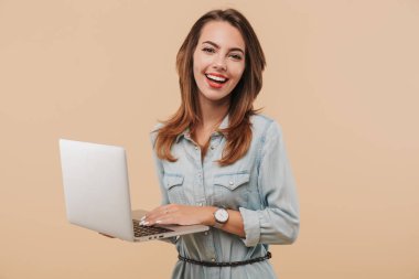 Bej renkli arka plan üzerinde izole dizüstü bilgisayar kullanan yaz giysileri mutlu bir genç kız portresi