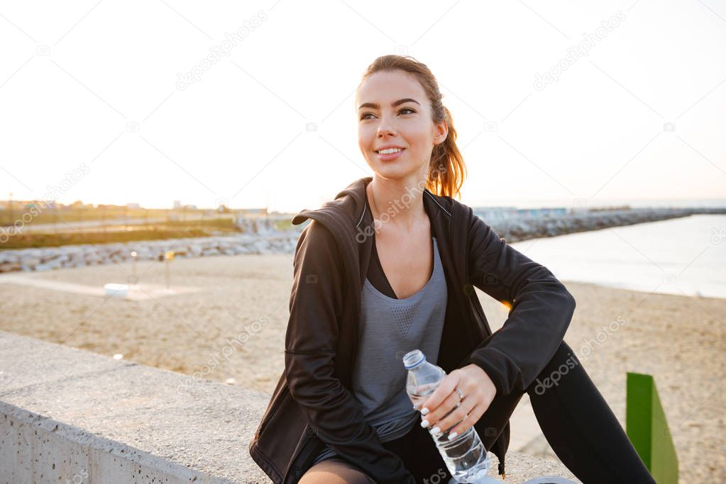 Image of happy beautiful young sports woman drinking water outdoors on the street.