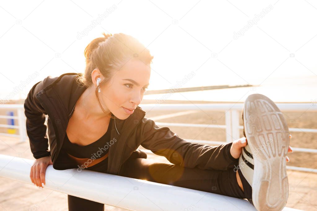 Image of young sports woman make stretching exercises outdoors on the street listening music.