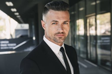 Takım elbise duran cam bina dışında büyüleyici bir genç işadamı portresi giymiş