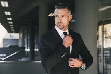 Yakışıklı bir genç işadamı portresi cam binanın önünde duran ve kravatını dokunmadan takım elbise giymiş