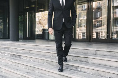 Bir cam bina dışında merdivenlerden aşağı yürüyüş takım elbise giymiş bir işadamı resim kırpılmış