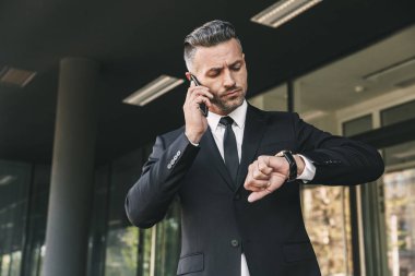 Yakışıklı bir genç işadamı portresi cam binanın önünde duran ve cep telefonu üzerinde konuşurken takım elbise giymiş